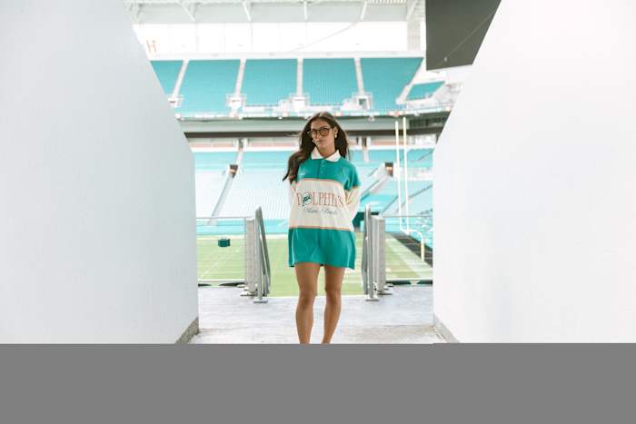 A woman models Miami Dolphins apparel in a football stadium.